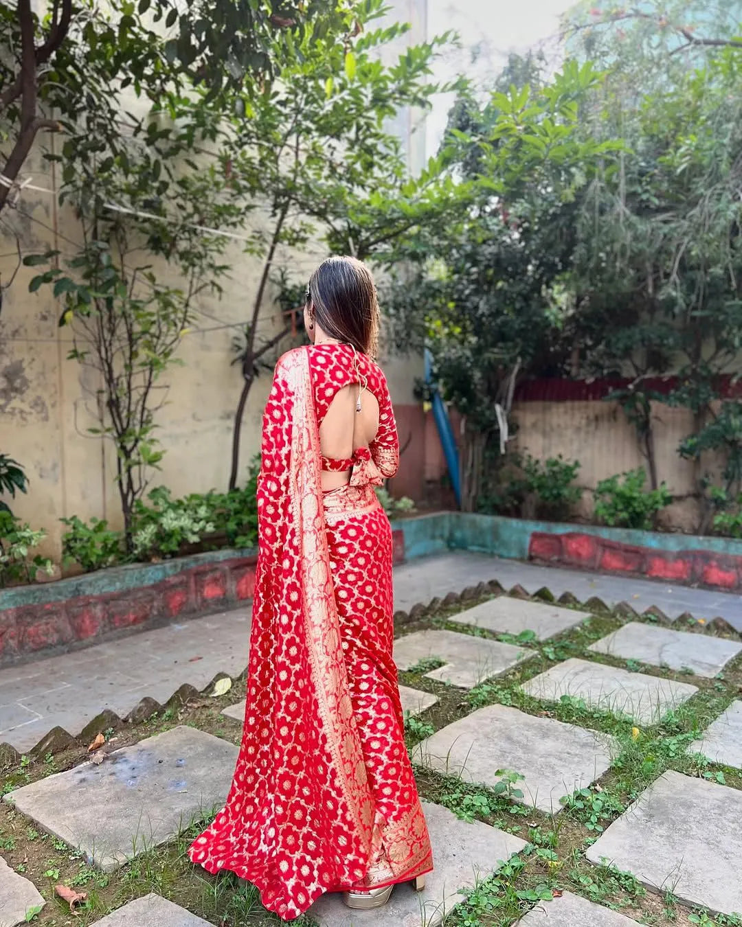 Woman wearing a red viscose georgette saree with golden zari embroidery, styled with matching jewelry and a graceful traditional look.