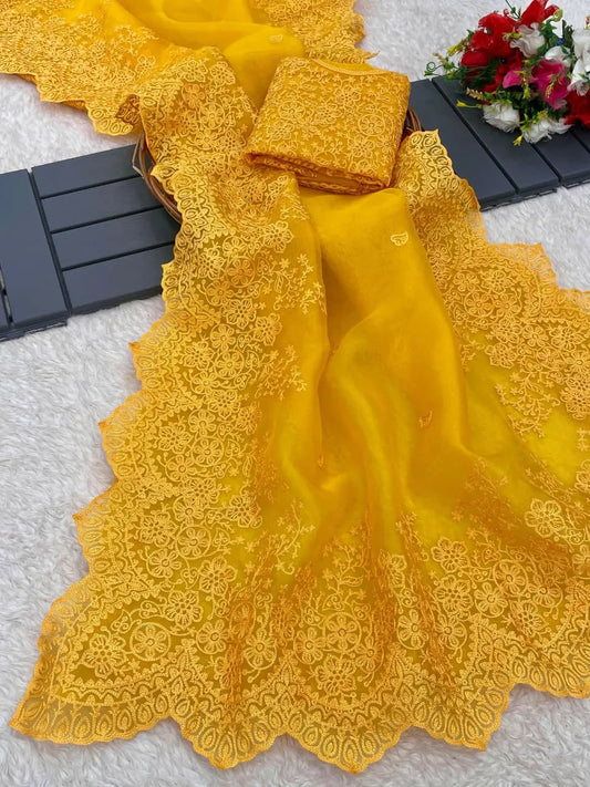 Mustard yellow organza saree with sleeveless embroidered blouse design featuring ornate lacework and grey studio backdrop