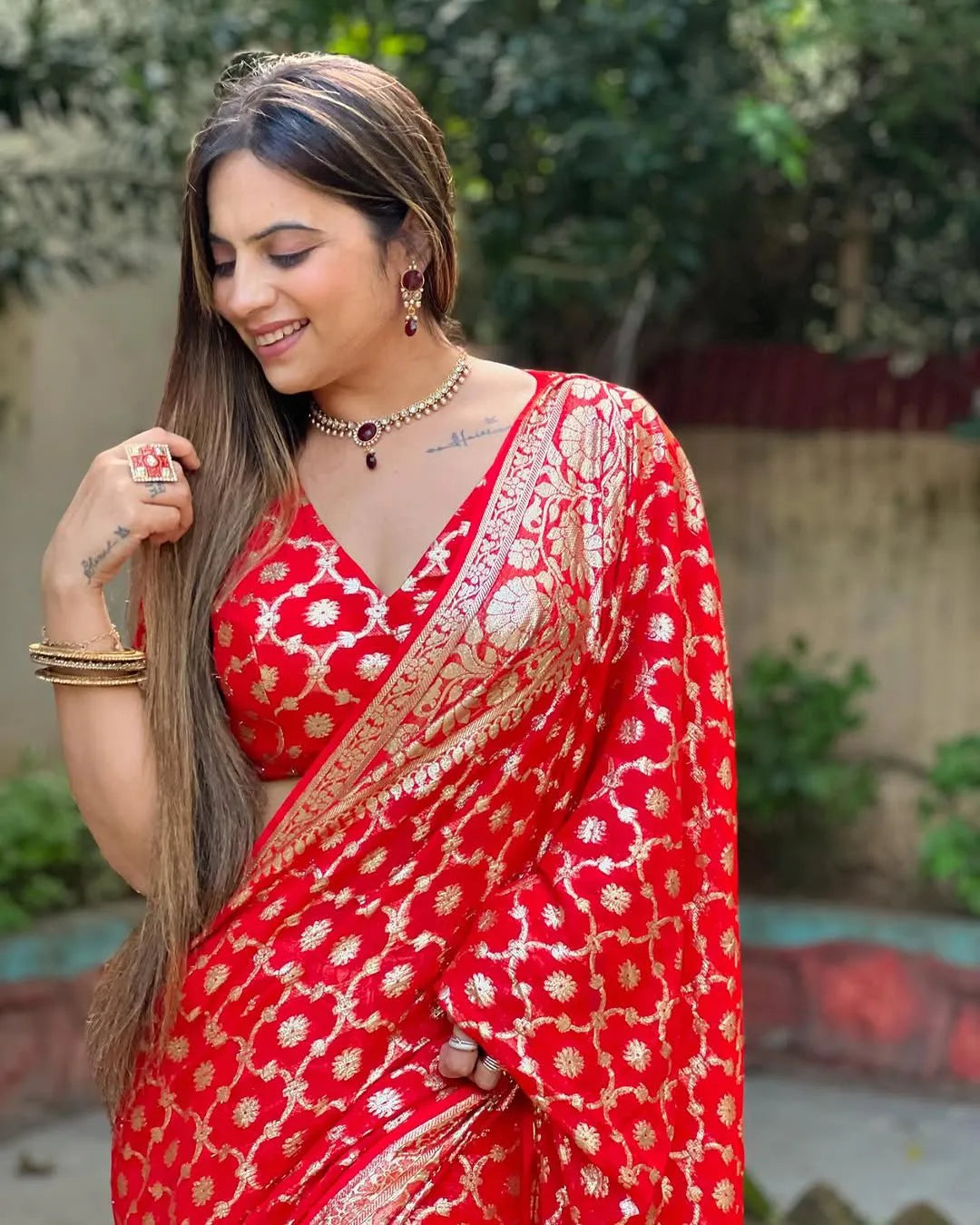 Woman wearing a red viscose georgette saree with golden zari embroidery, styled with matching jewelry and a graceful traditional look.