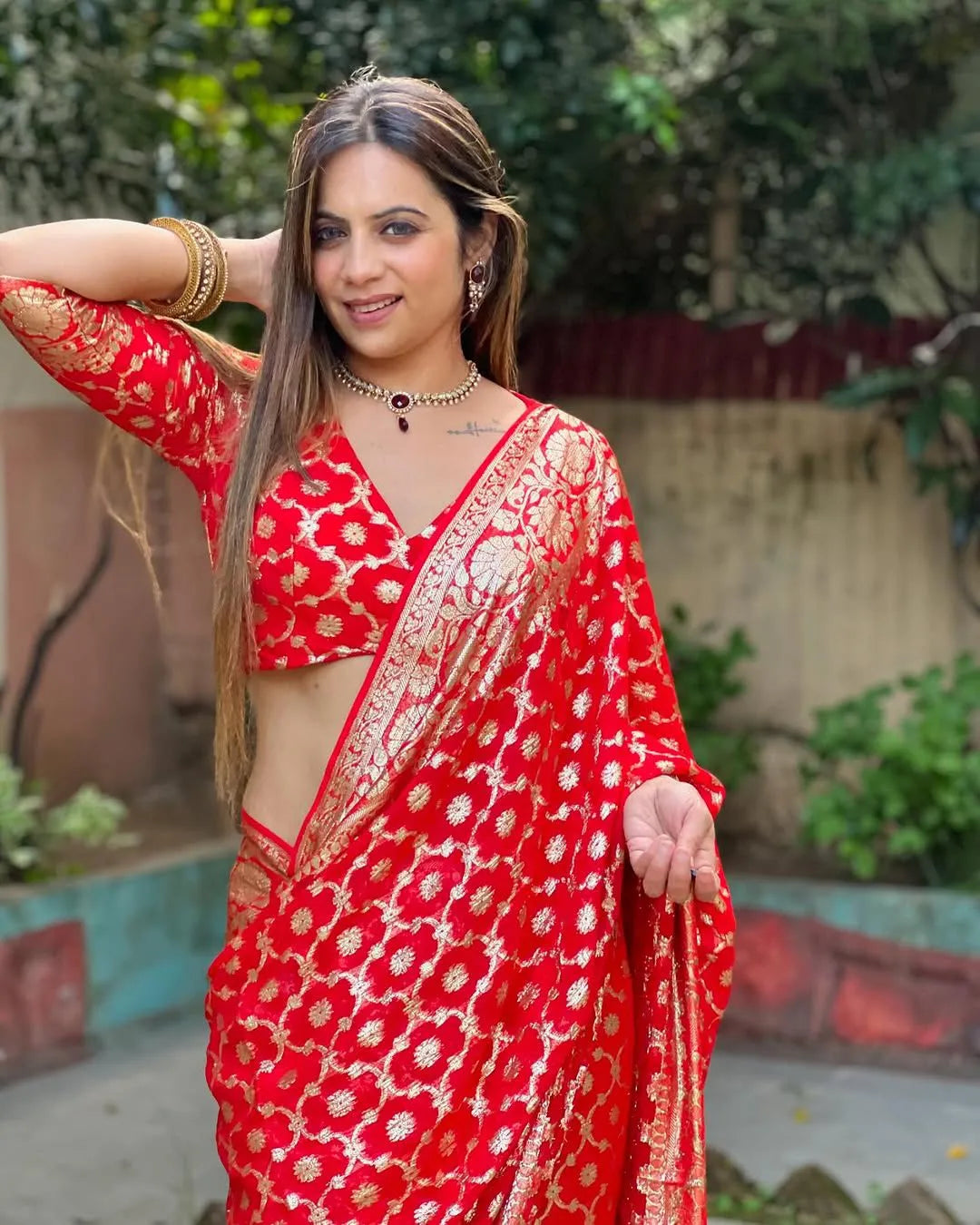 Woman wearing a red viscose georgette saree with golden zari embroidery, styled with matching jewelry and a graceful traditional look.
