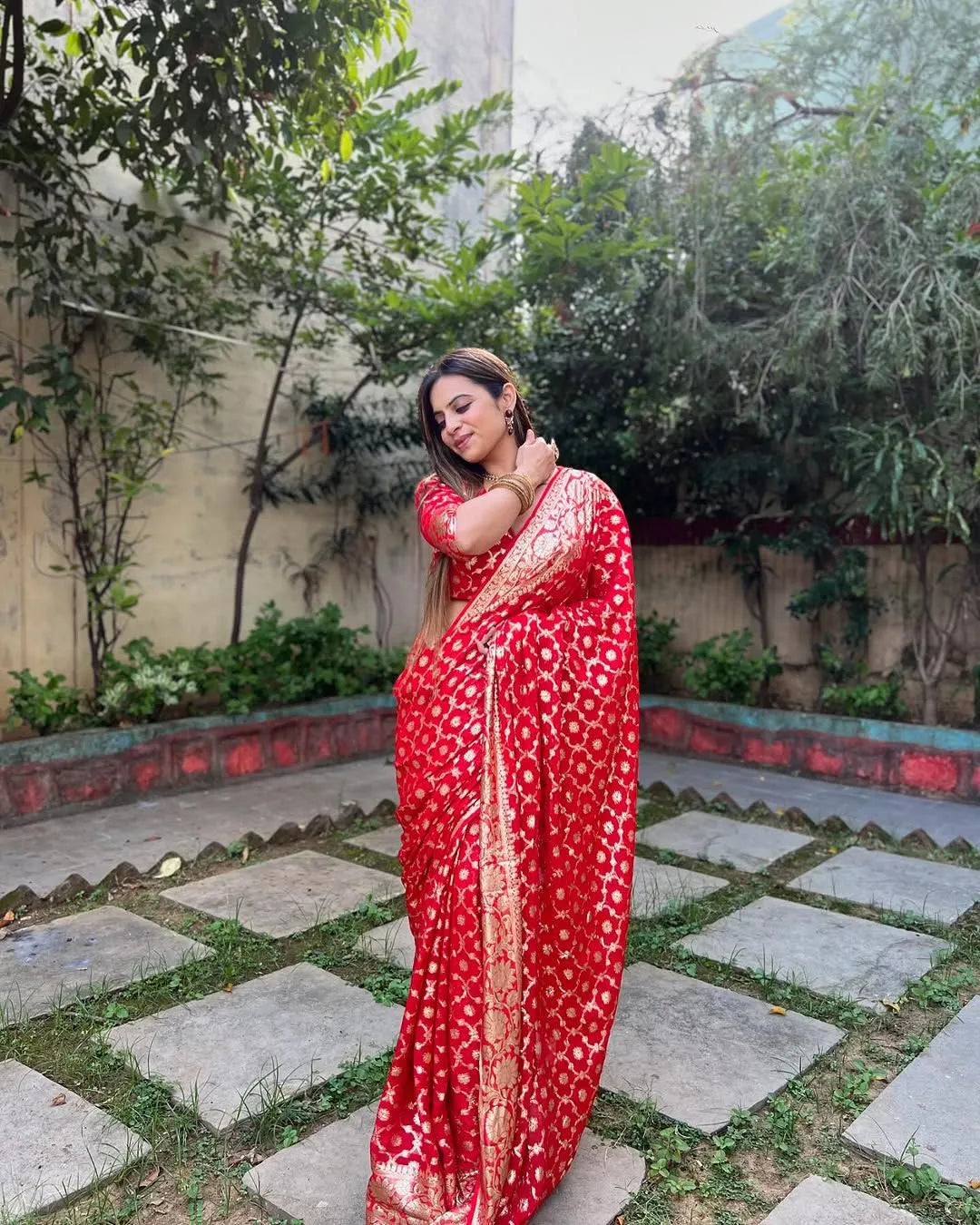 Woman wearing a red viscose georgette saree with golden zari embroidery, styled with matching jewelry and a graceful traditional look.