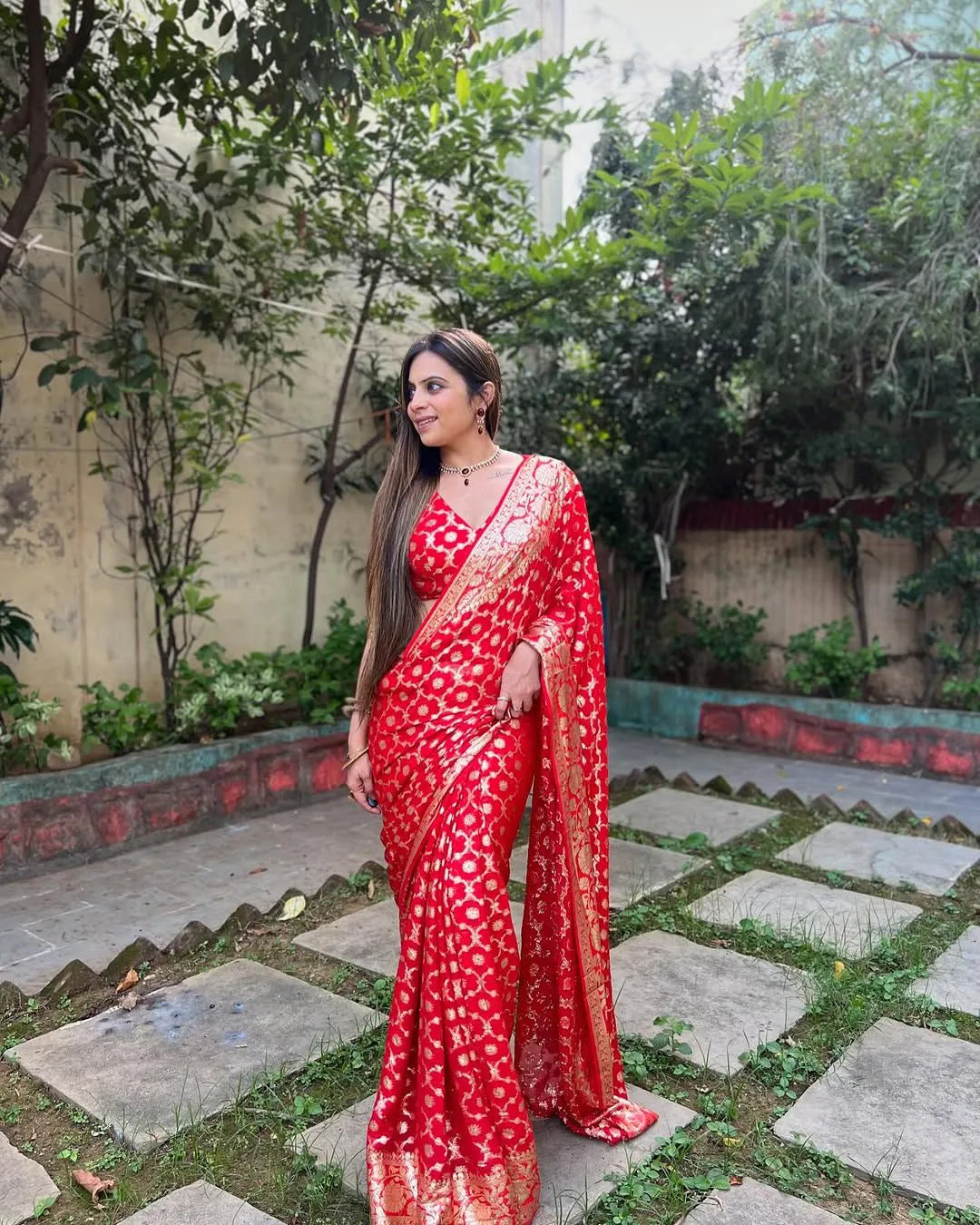 Woman wearing a red viscose georgette saree with golden zari embroidery, styled with matching jewelry and a graceful traditional look.