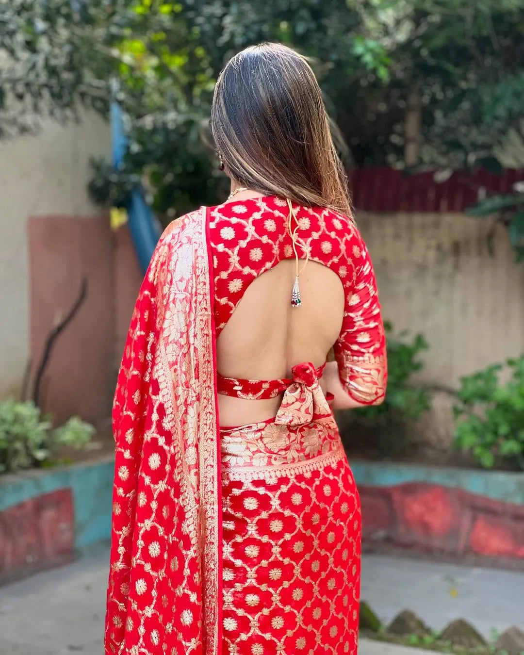 Woman wearing a red viscose georgette saree with golden zari embroidery, styled with matching jewelry and a graceful traditional look.