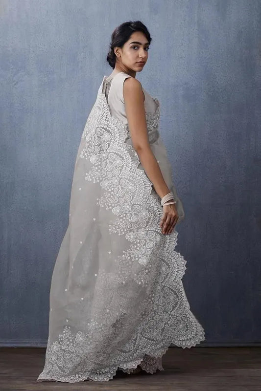 White organza saree with sleeveless embroidered blouse design featuring intricate lace border and minimal studio backdrop