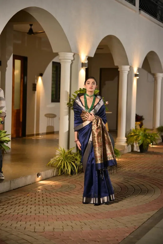 Navy blue tussar silk saree with golden zari border and ornate brocade pallu displayed on model in elegant colonial architecture setting