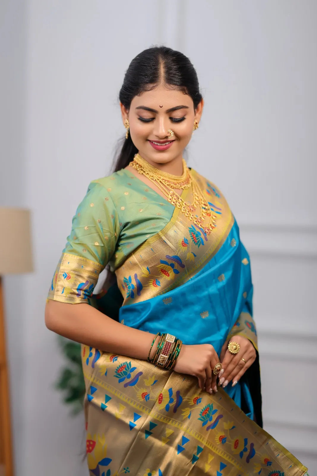 Traditional paithani saree look featuring peacock blue silk saree with golden zari border and colorful peacock motifs styled with gold jewelry