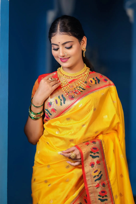 Traditional paithani saree look in bright yellow silk with orange-red border, colorful floral motifs, styled with layered gold jewelry