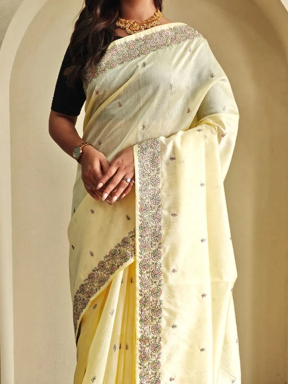 Woman wearing pastel yellow tussar silk saree with embroidered floral border and black blouse accessorized with gold choker necklace