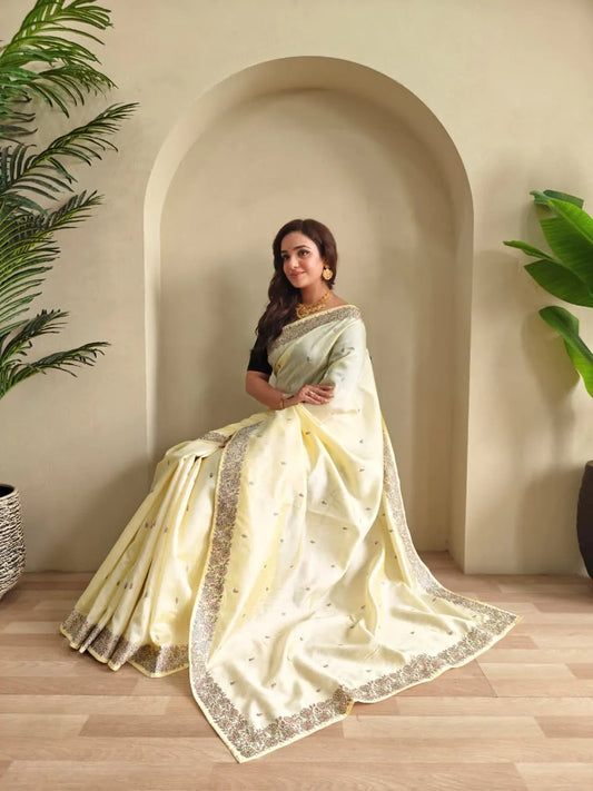 Woman wearing pastel yellow tussar silk saree with embroidered floral border and black blouse accessorized with gold choker necklace