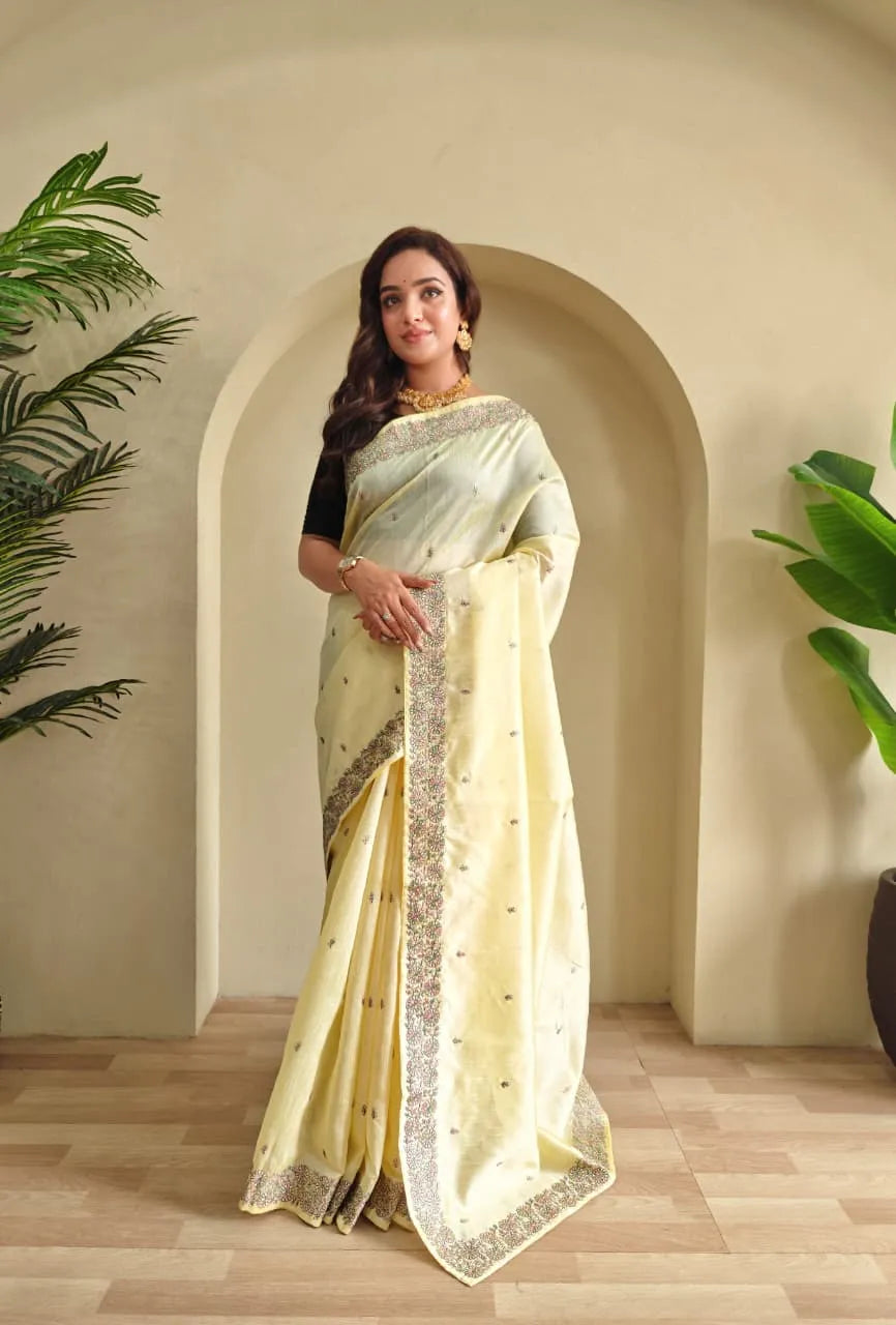 Woman wearing pastel yellow tussar silk saree with embroidered floral border and black blouse accessorized with gold choker necklace