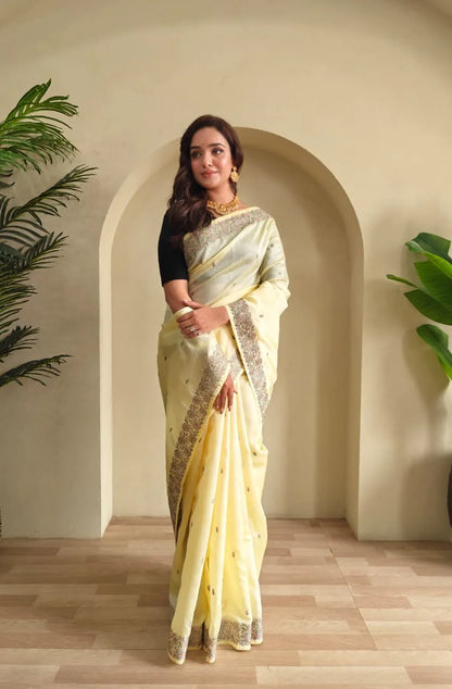 Woman wearing pastel yellow tussar silk saree with embroidered floral border and black blouse accessorized with gold choker necklace