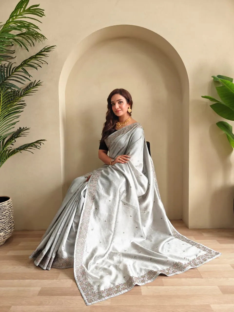 Silver tussar saree with sequined embroidered border paired with black elbow-length blouse and gold choker necklace