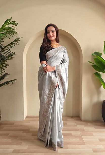Silver tussar saree with sequined embroidered border paired with black elbow-length blouse and gold choker necklace