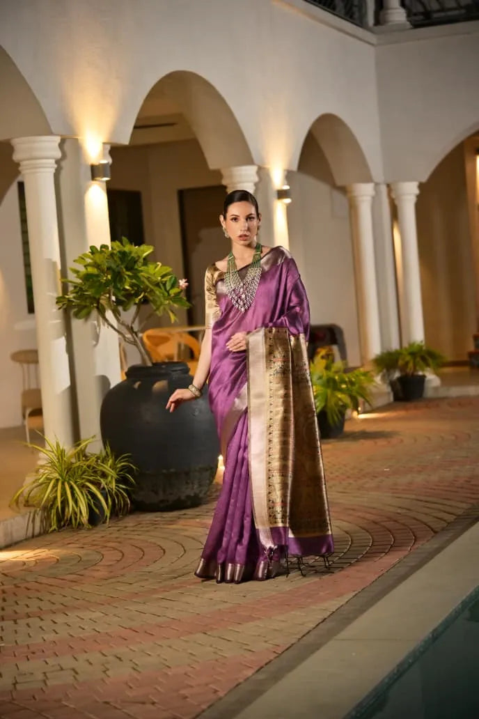 Purple tussar silk saree with golden border and ornate pallu displayed on model in traditional architectural setting with white pillars and arches