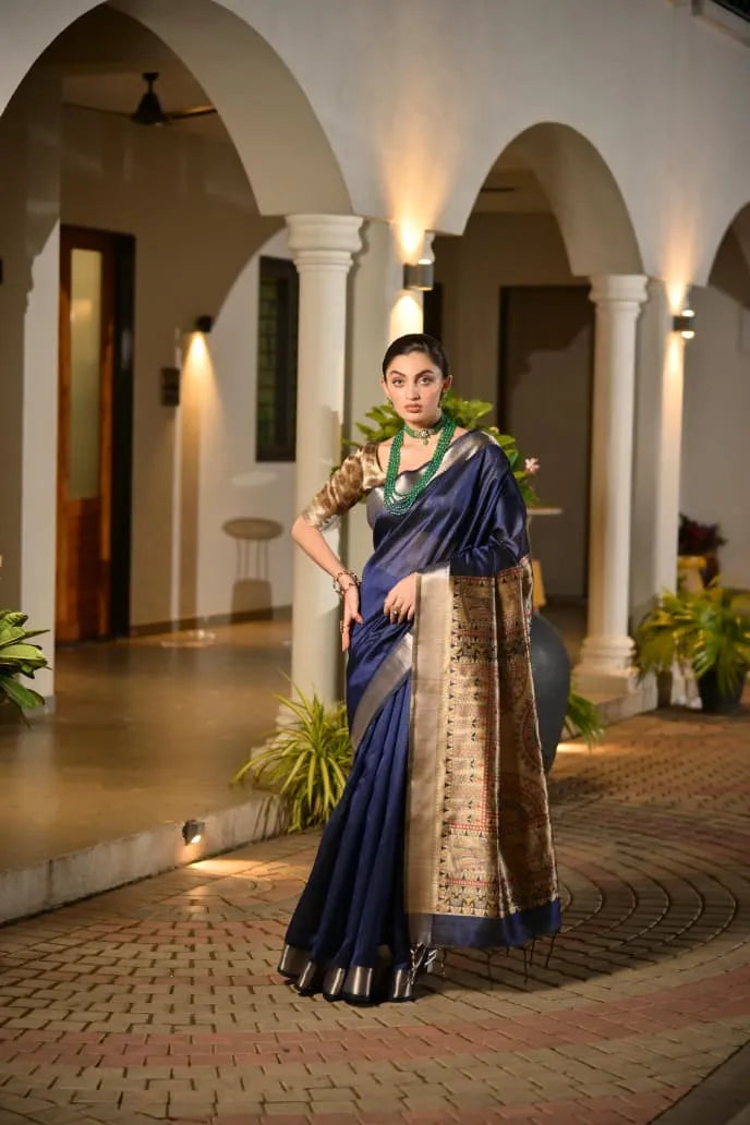 Navy blue tussar silk saree with golden zari border and ornate brocade pallu displayed on model in elegant colonial architecture setting