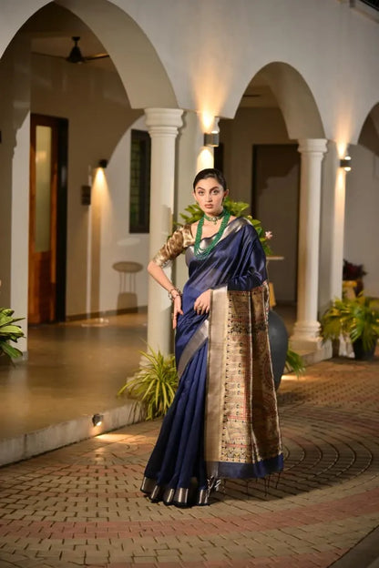 Navy blue tussar silk saree with golden zari border and ornate brocade pallu displayed on model in elegant colonial architecture setting