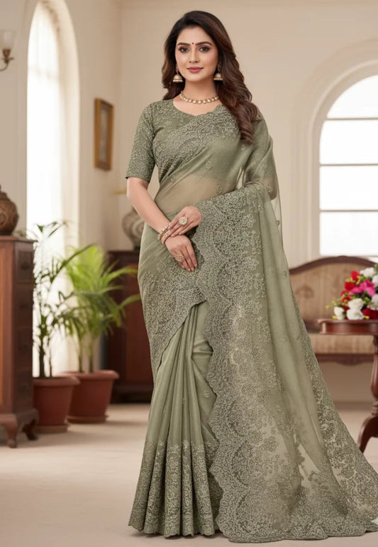 Sage green organza saree with embroidered blouse design featuring intricate lacework and elegant interior setting